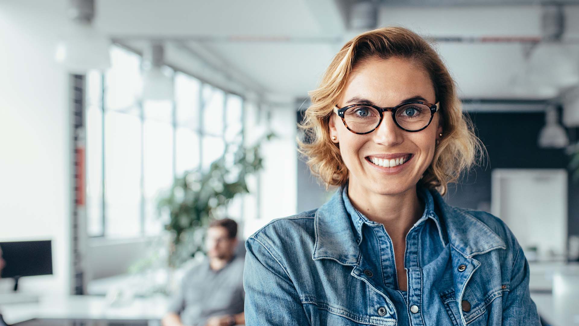 A smiling woman with glasses in an office.