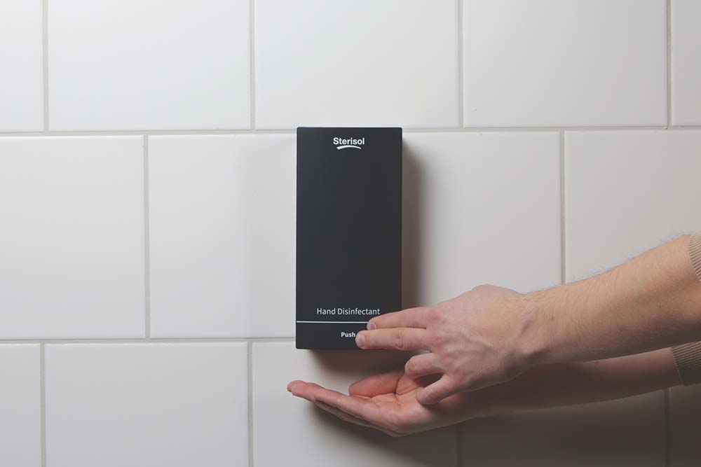 En svart dispenser monterad på en vit kaklad vägg