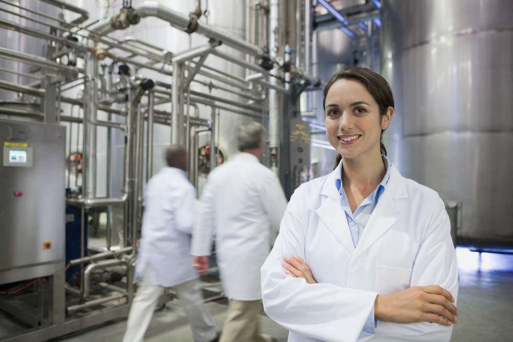 A happy woman wearing a white lab coat in a factory
